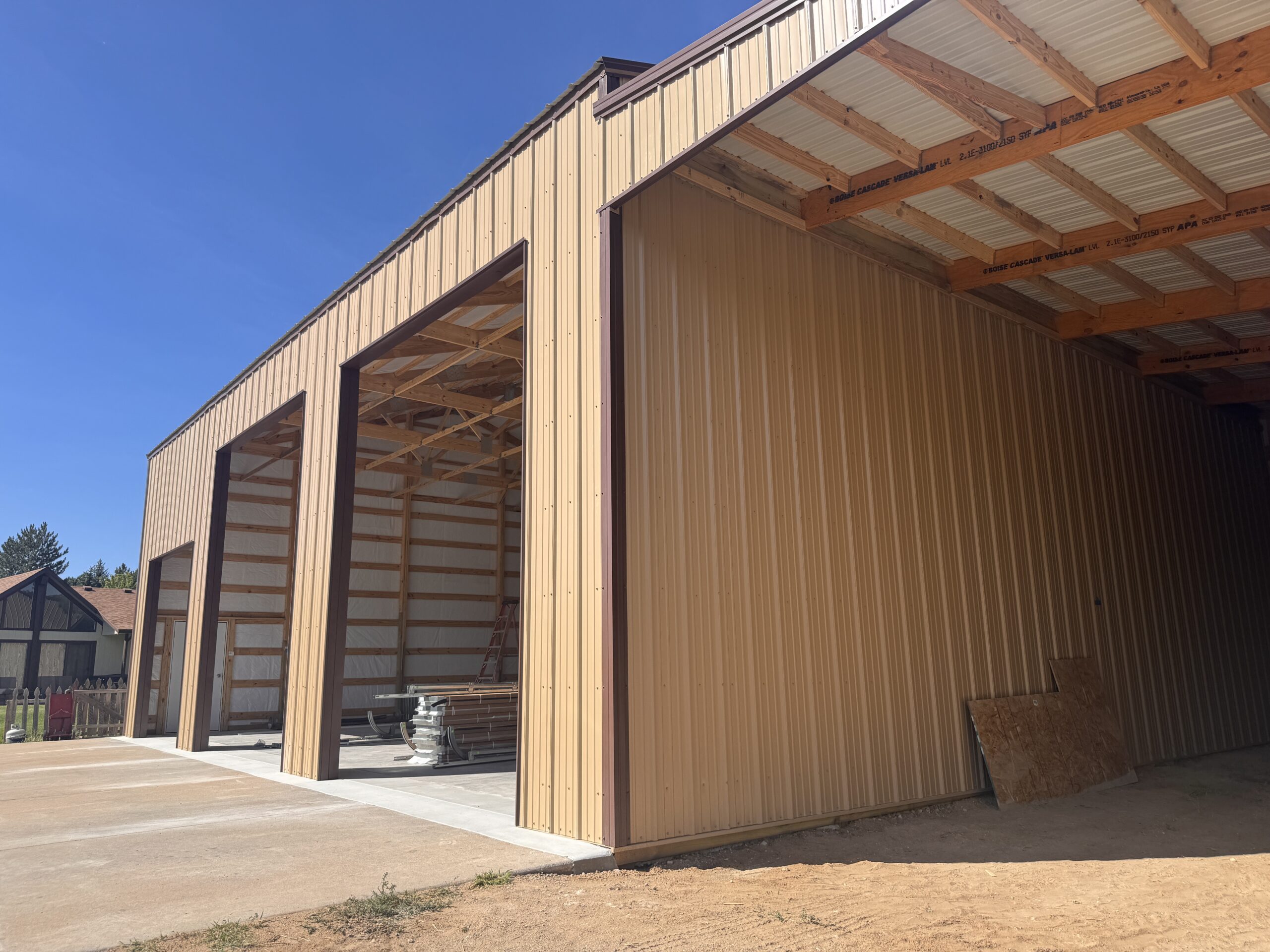 A tan metal building under construction, featuring large open bays.
